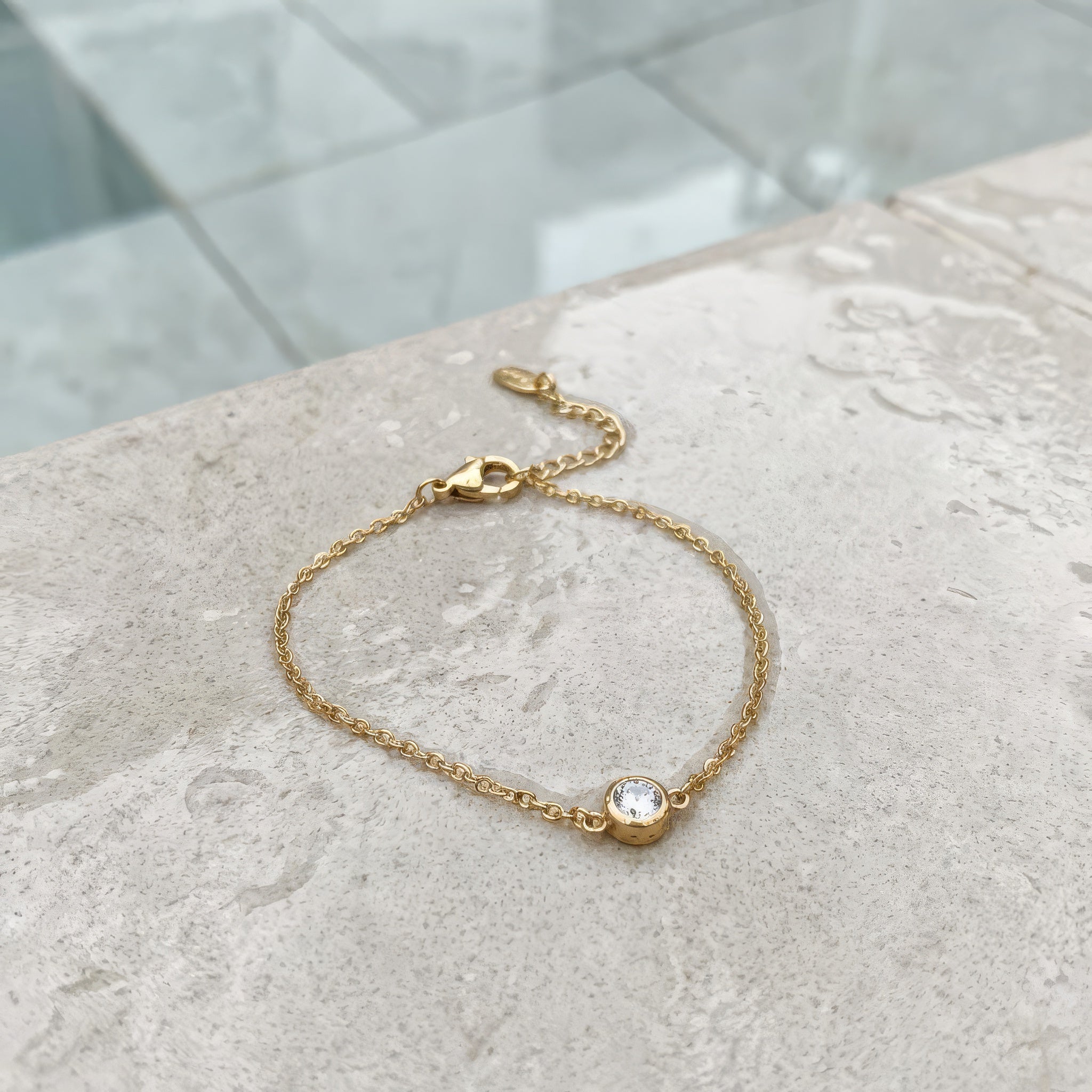 Gold bracelet with a small round gemstone on a textured surface