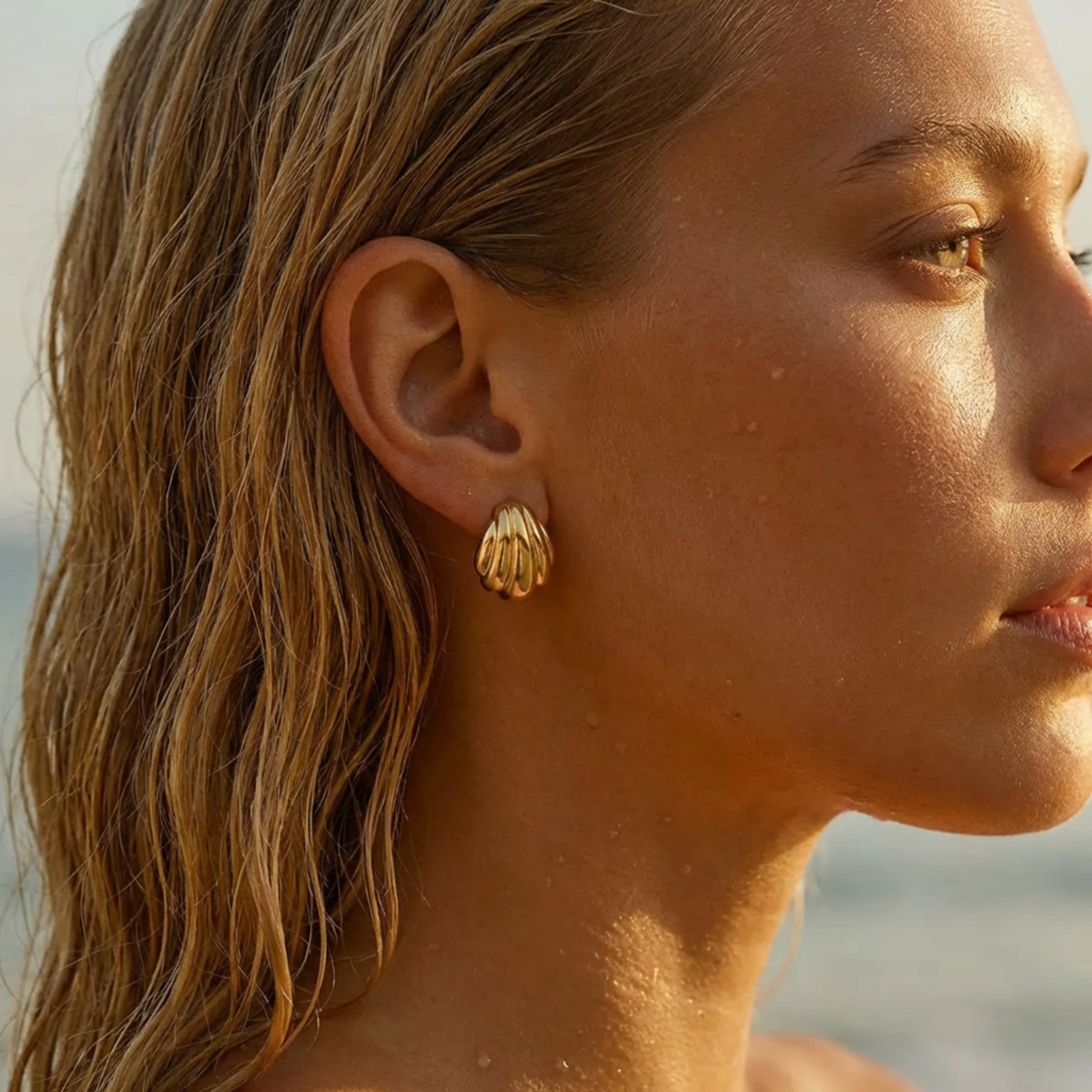 Close-up of a woman wearing gold earrings with a blurred beach background