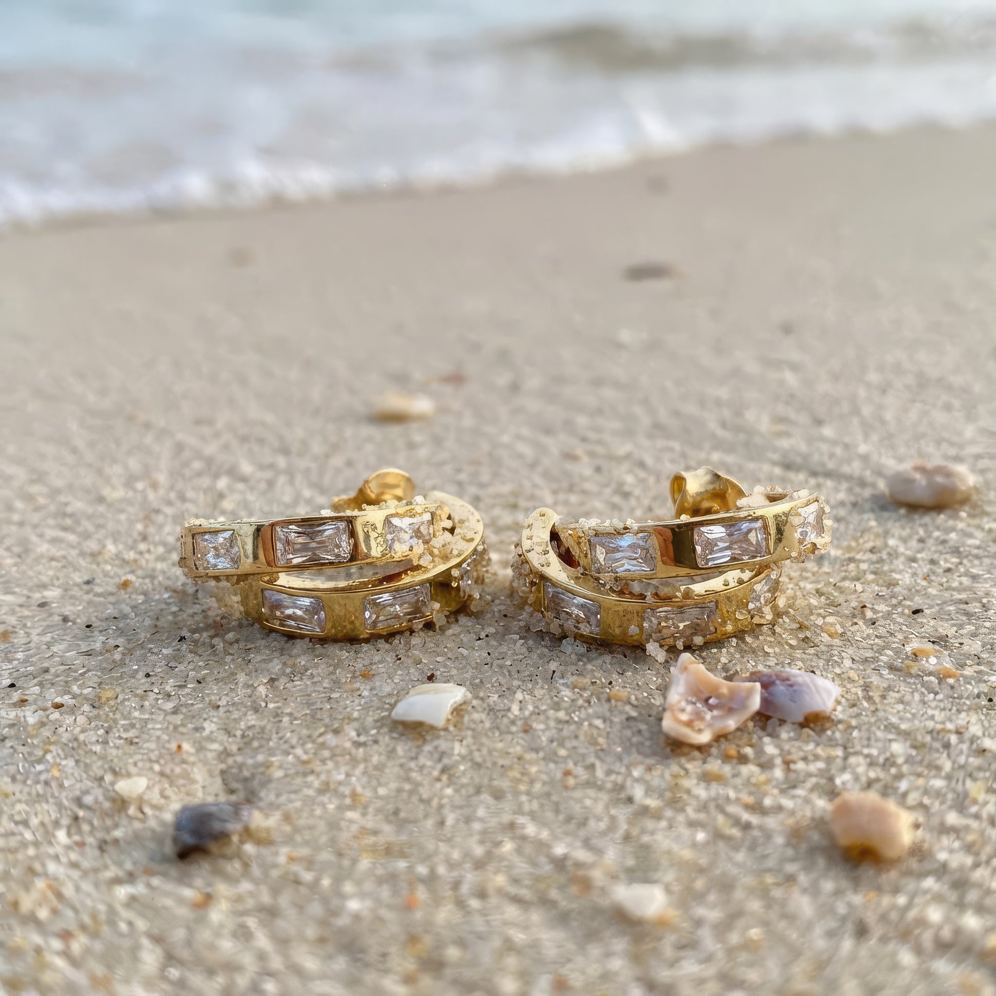 Gold hoop earrings in the sand at the beach 