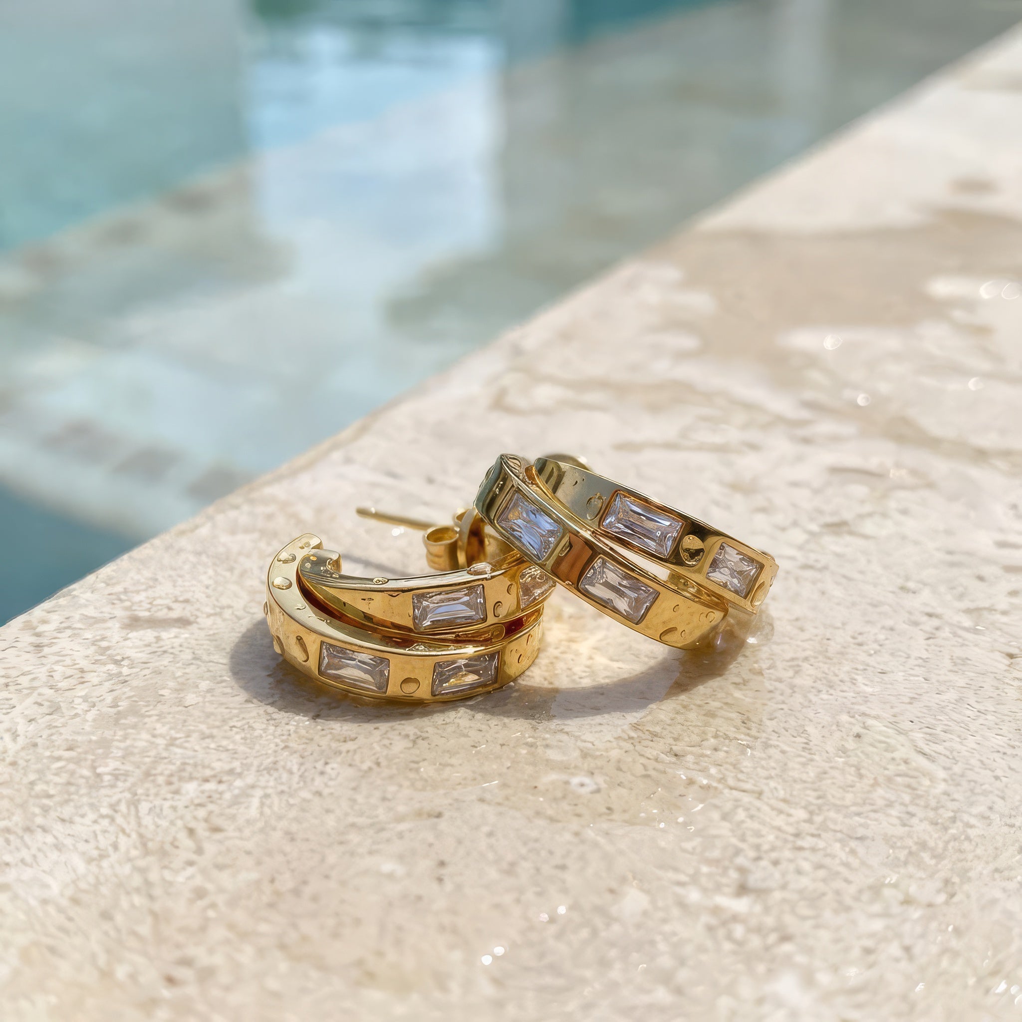 Gold hoop earrings on a wet surface on th edge of a pool