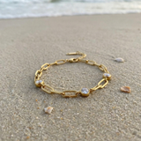 Gold chain bracelet with three diamond-like stones lying in the sand on the beach with the ocean in the background