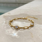 Gold chain bracelet with three diamond-like stones lying on a stone surface on the edge of a pool