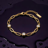 Gold chain bracelet with three diamond-like stones on a wet dark purple surface