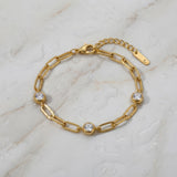 Gold chain bracelet with three diamond-like stones on a wet white marble surface