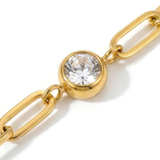 Close up of white gemstone on a gold chain bracelet on a white background