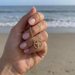 Gold cross necklace with rhinestones held in hand in front of the ocean