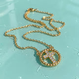 Gold cross necklace with rhinestones on a wet turquoise surface