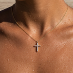 A gold chain necklace with a small cross pendant set with clear stones, worn on a person's neck and upper chest.