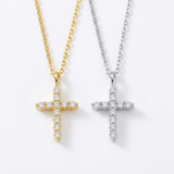 Two cross pendant necklaces, one in gold and one in silver, both adorned with clear round-cut gemstones, suspended from a matching gold chain and silver chain against a plain white background.against a white background. 