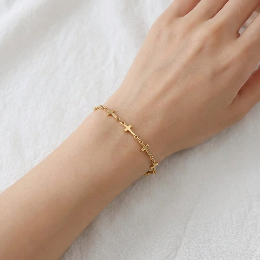 Gold bracelet with links made of mini crosses on a wrist against a white background
