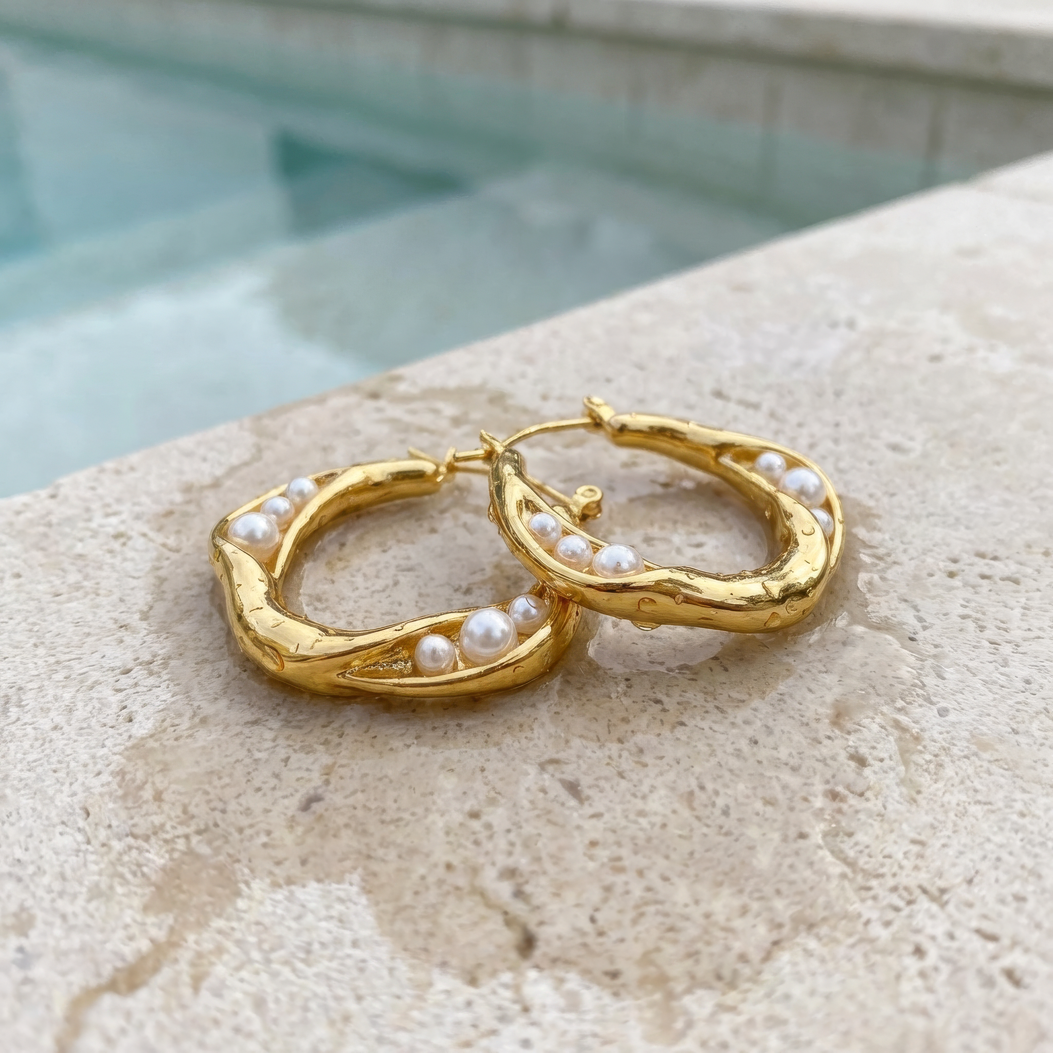 Gold hoop earrings with pearls on a stone surface