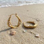 Gold hoop earrings with pearls on a sandy beach
