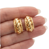 Gold hoop earrings held between fingers on a white background