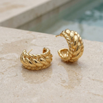 Gold hoop earrings on a textured surface of the edge of a pool with a blurred pool filled with water in the background.