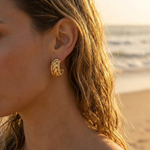 Close-up of a woman wearing a gold earring with a beach in the background