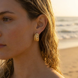 Close-up of a woman wearing gold earrings with a beach background