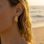 Close-up of a woman wearing gold hoop earrings with a beach background
