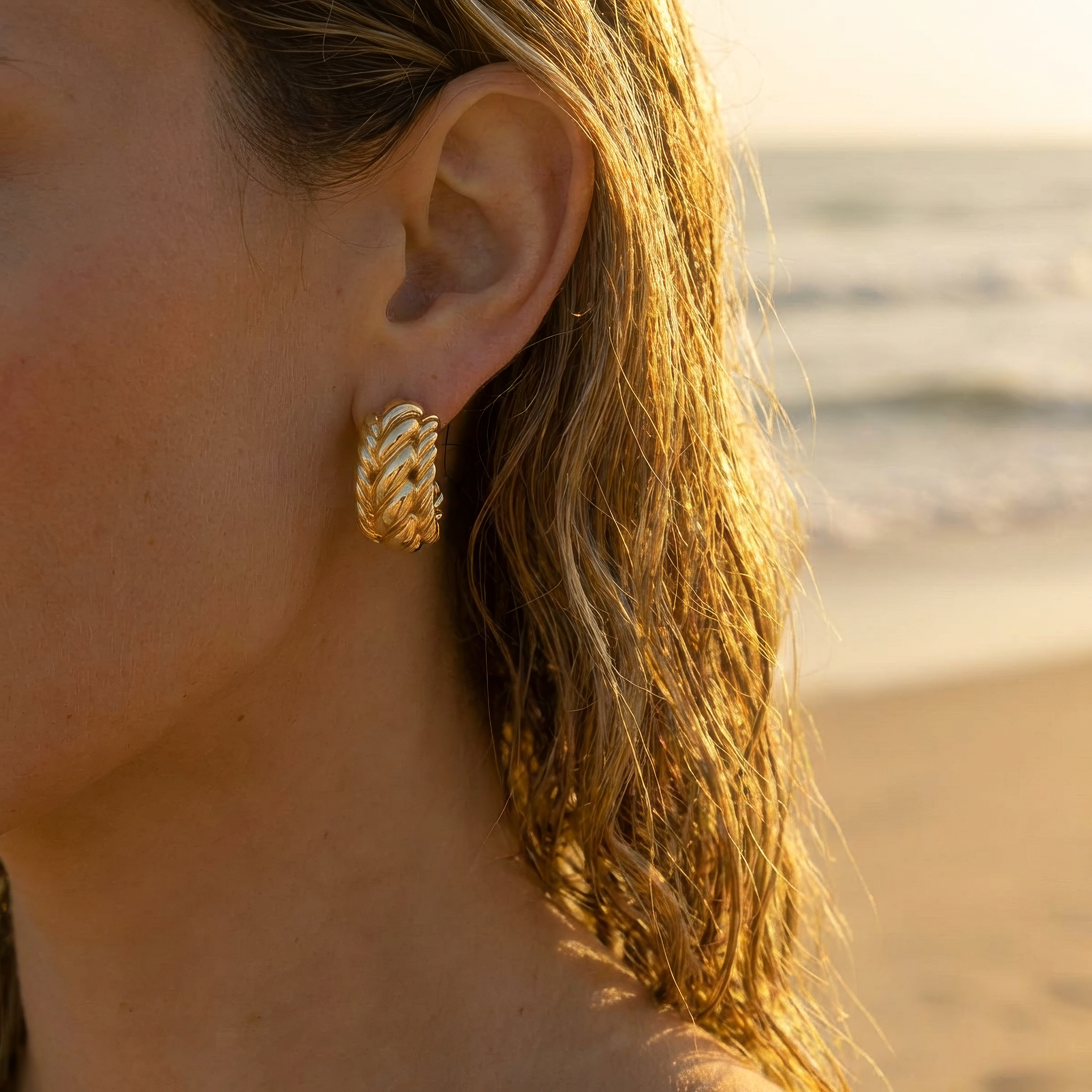 Close-up of a woman wearing gold hoop earrings with a beach background