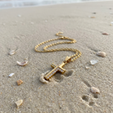 Gold cross necklace on sand with ocean in the background