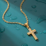 Gold cross necklace with clear stones on a teal surface with water droplets