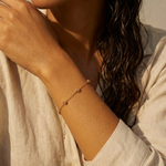 A woman wearing a gold bracelet with five stationary gold rosebud designs spaced out on the chain with a neutral background