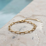 Gold paperclip chain bracelet on a wet stone surface at the edge of a pool