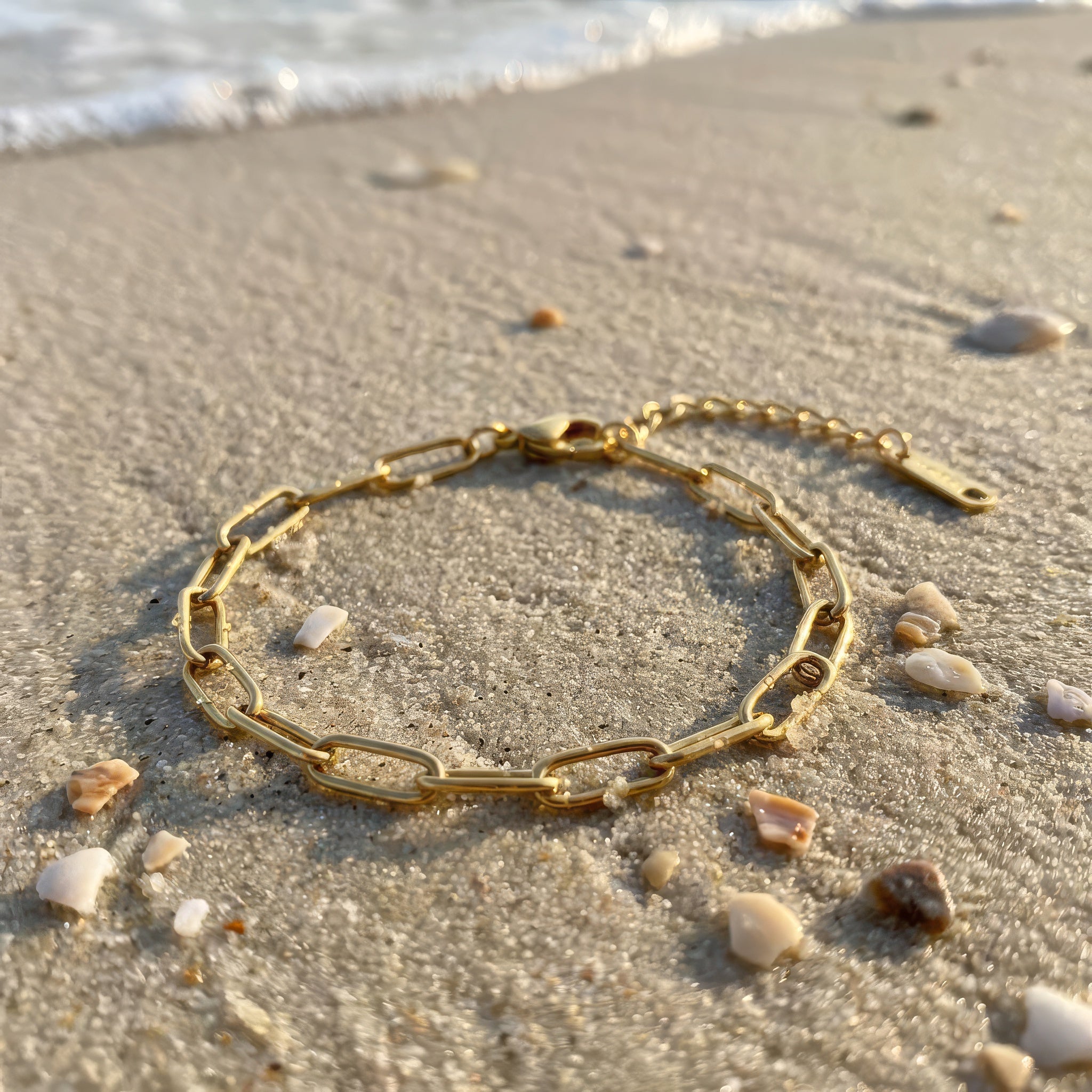 Gold paperclip chain bracelet on the wet sand at the beach with the ocean nearb in the background