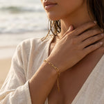 Woman wearing a gold paperclip chain bracelet on her wrist at the ocean