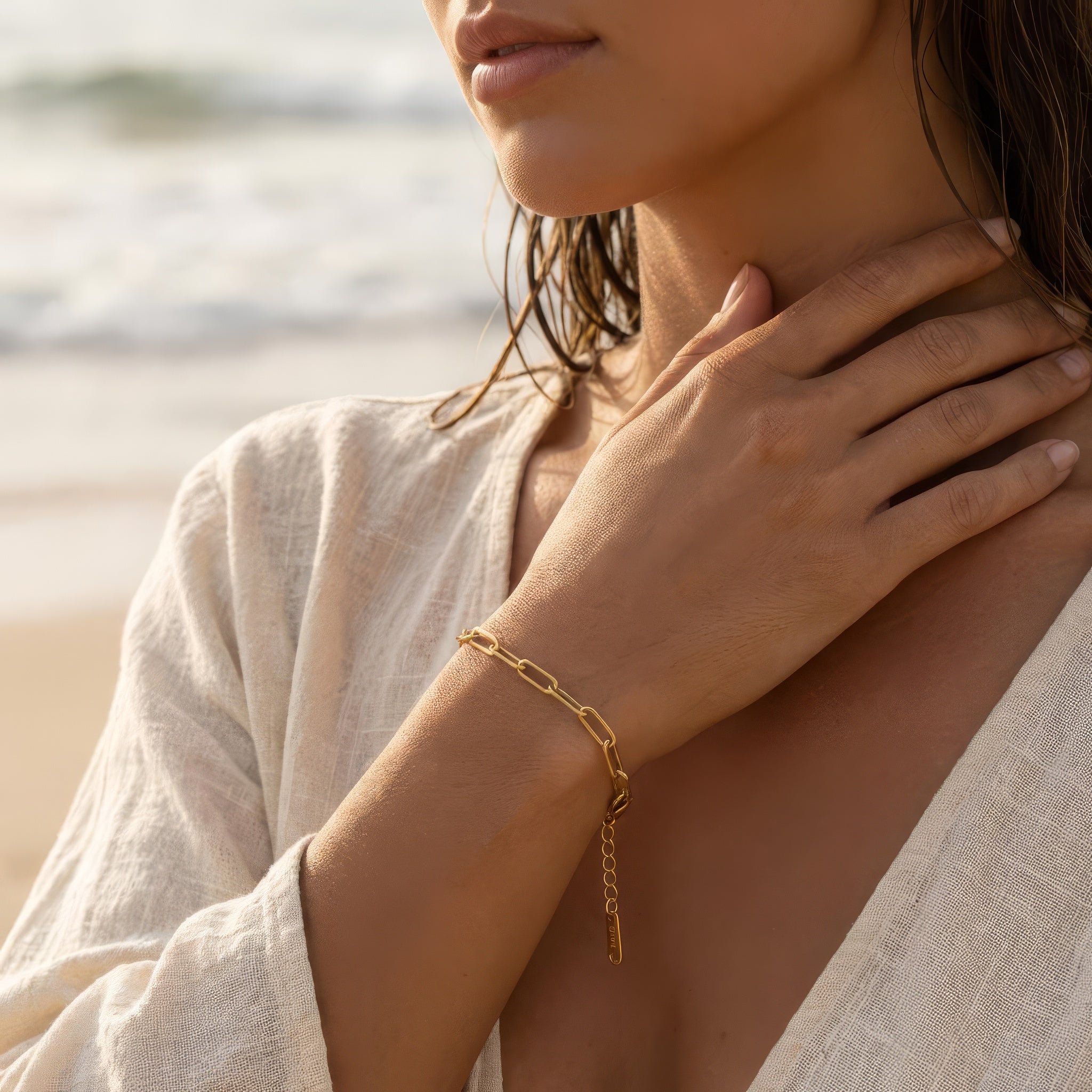 Woman wearing a gold paperclip chain bracelet on her wrist at the ocean