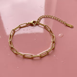 Gold paperclip chain bracelet on a wet pink surface