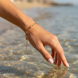 Gold paperclip chain bracelet on a woman's wrist above the ocean