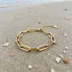 Gold paperclip chain bracelet lying on wet sand at the ocean