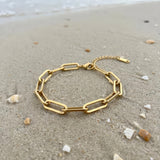 Gold paperclip chain bracelet lying on wet sand at the ocean