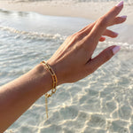 Gold paperclip chain bracelet on a woman's write above the ocean