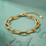 Gold paperclip chain bracelet on a wet mint green surface