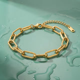 Gold paperclip chain bracelet on a wet mint green surface