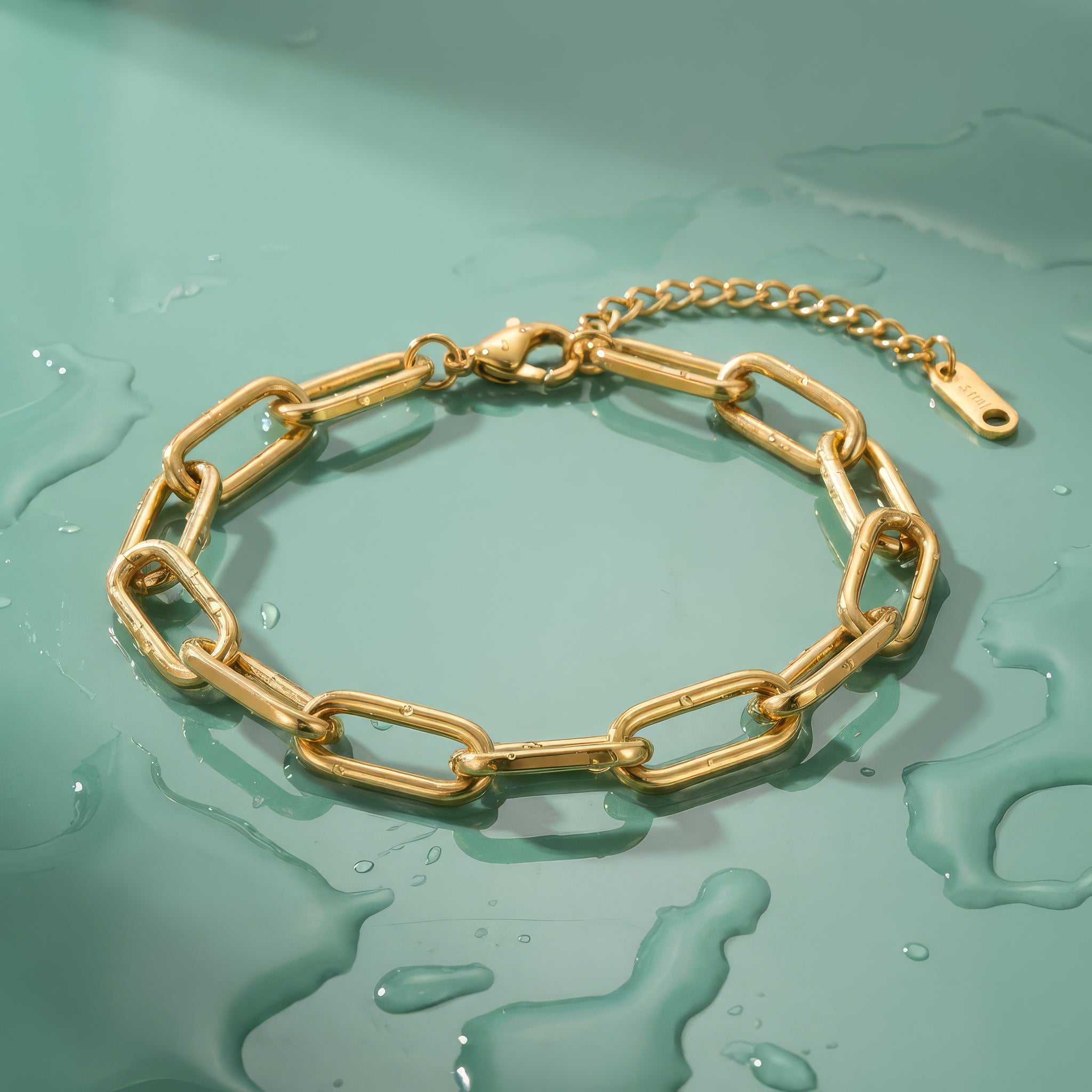 Gold paperclip chain bracelet on a wet mint green surface